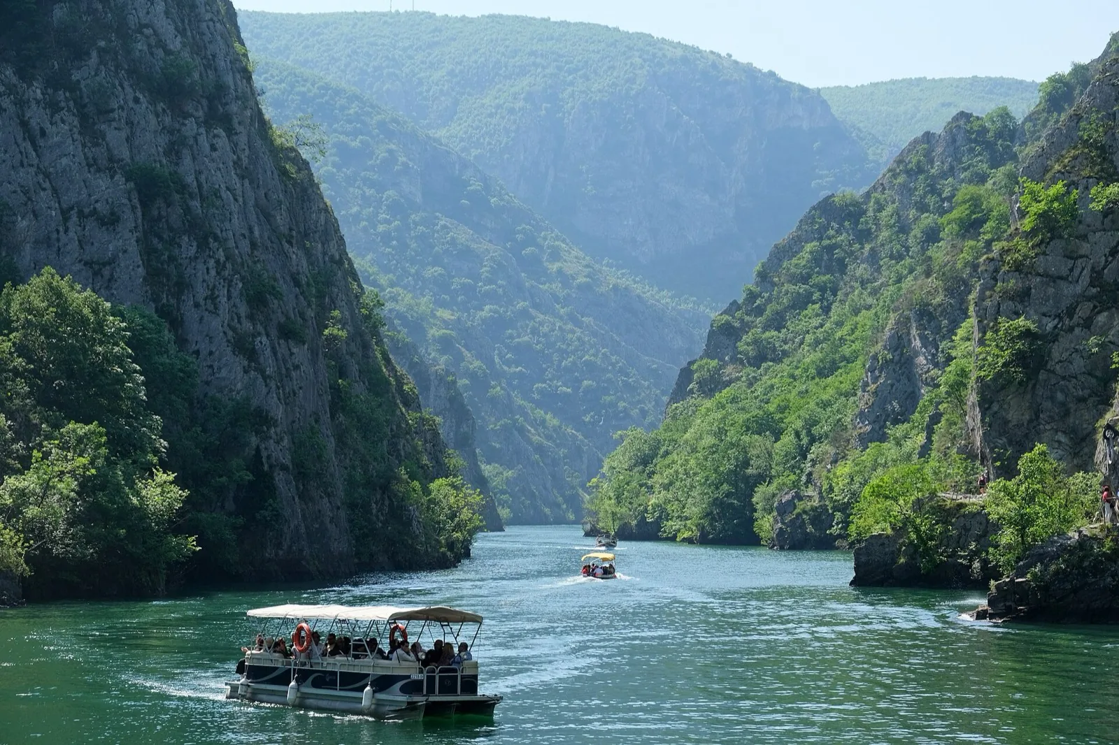 Tour boats gliding through Matka Canyon between green cliffs